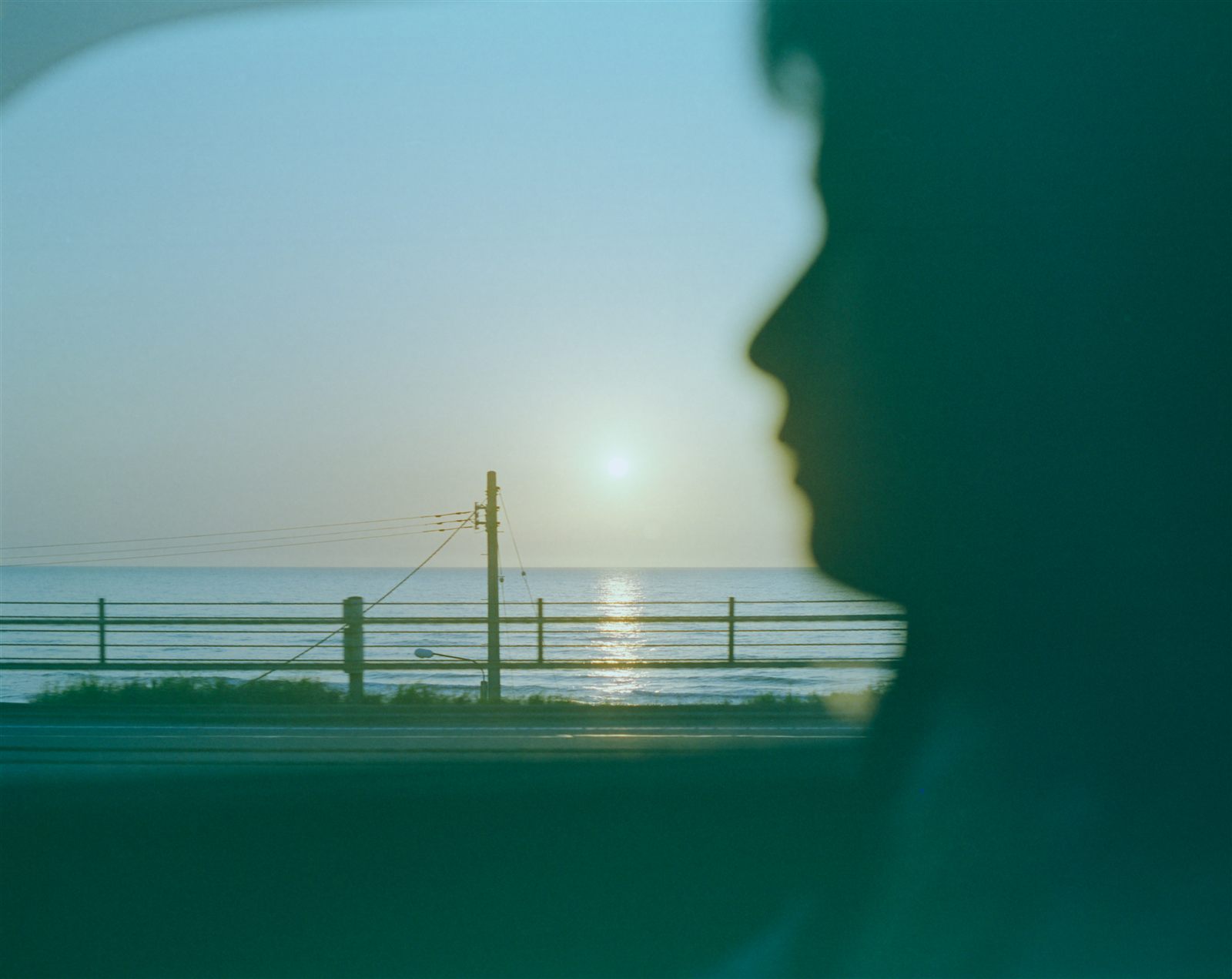 電車の窓の外に広がる海と朝日　手前に人の横顔の影